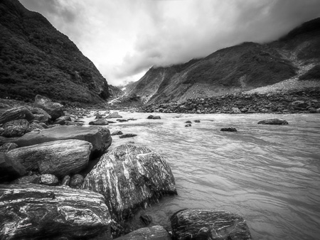 Franz Josef Glacier valley view in B/W from Waiho river with large boulders in the foreground.